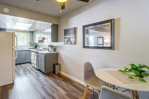 A modern kitchen with stainless steel appliances, a dining area with a round table and chairs, and a small trash bin. - Central Folsom Condo: Walk to Parks & Dining (Folsom)