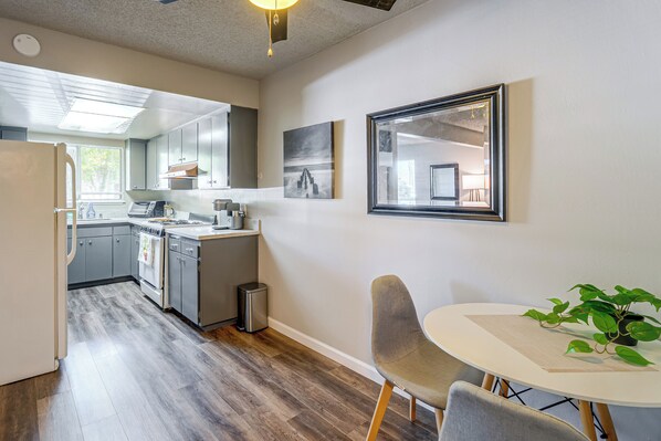 A modern kitchen with stainless steel appliances, a dining area with a round table and chairs, and a small trash bin.