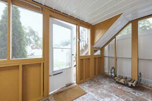 A room with wooden walls, a white door, and large windows. There is a doormat and a stack of firewood outside. - Comfy & Cozy Home Close to Penn State! (Pleasant Gap)