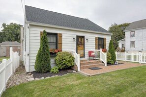 Une maison de plain-pied avec un porche à l’avant, un petit jardin et une clôture blanche en bois.