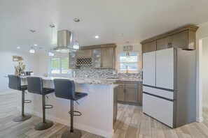 A modern kitchen with a marble countertop, stainless steel appliances, and a bar area with stools. - Half-Acre Yard, Modern Interior! Aurora Home (Aurora)