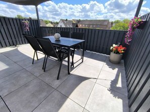 An outdoor patio with a table and chairs, a potted plant, and a view of houses in the background. - Holiday Apartment With 1 Bedroom (Walsrode)