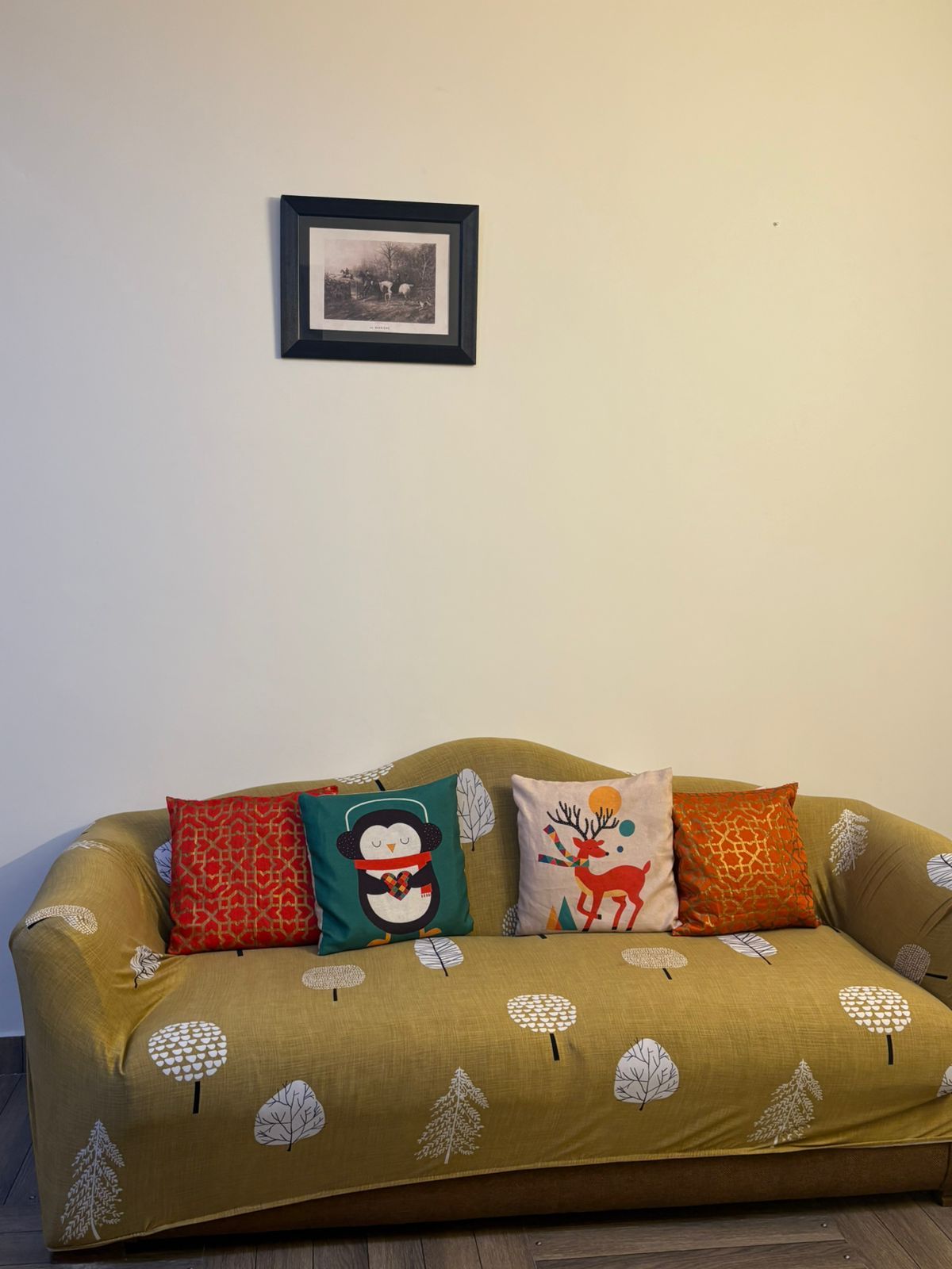 A sofa with a leaf pattern, a framed picture on the wall, and three decorative pillows.