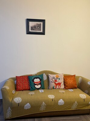 A sofa with a leaf pattern, a framed picture on the wall, and three decorative pillows. - Fabulous 3-bedroom floor with AC in vibrant Noida (Noida)