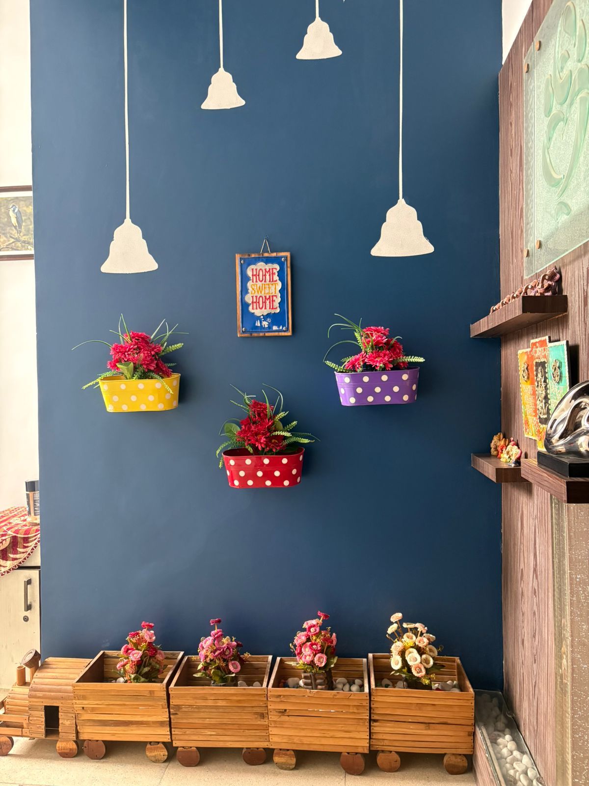 A room with a blue wall, hanging white pendant lights, and flower planters in yellow, red, and purple pots.