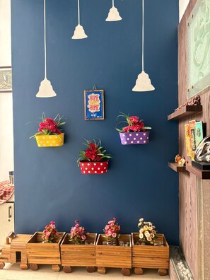 A room with a blue wall, hanging white pendant lights, and flower planters in yellow, red, and purple pots. - Fabulous 3-bedroom floor with AC in vibrant Noida (Noida)