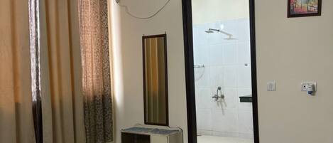 Habitación de hotel con cama, espejo, mesita, zona de ducha y un cuadro en la pared.