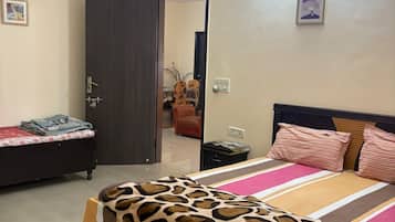 A bedroom with a bed, a nightstand, a door leading to another room, and a wall-mounted light fixture.