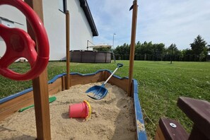A sandbox with a shovel and a bucket, surrounded by a wooden border. - Baltic Harmony Villas (Grzybowo)