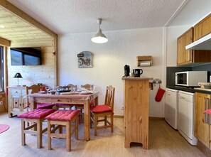 A cozy kitchen with wooden cabinets, a dining table with chairs, and a television mounted on the wall. - (BZ.55) 2-room apartment with mountain views, right at the slopes (Les Menuires)