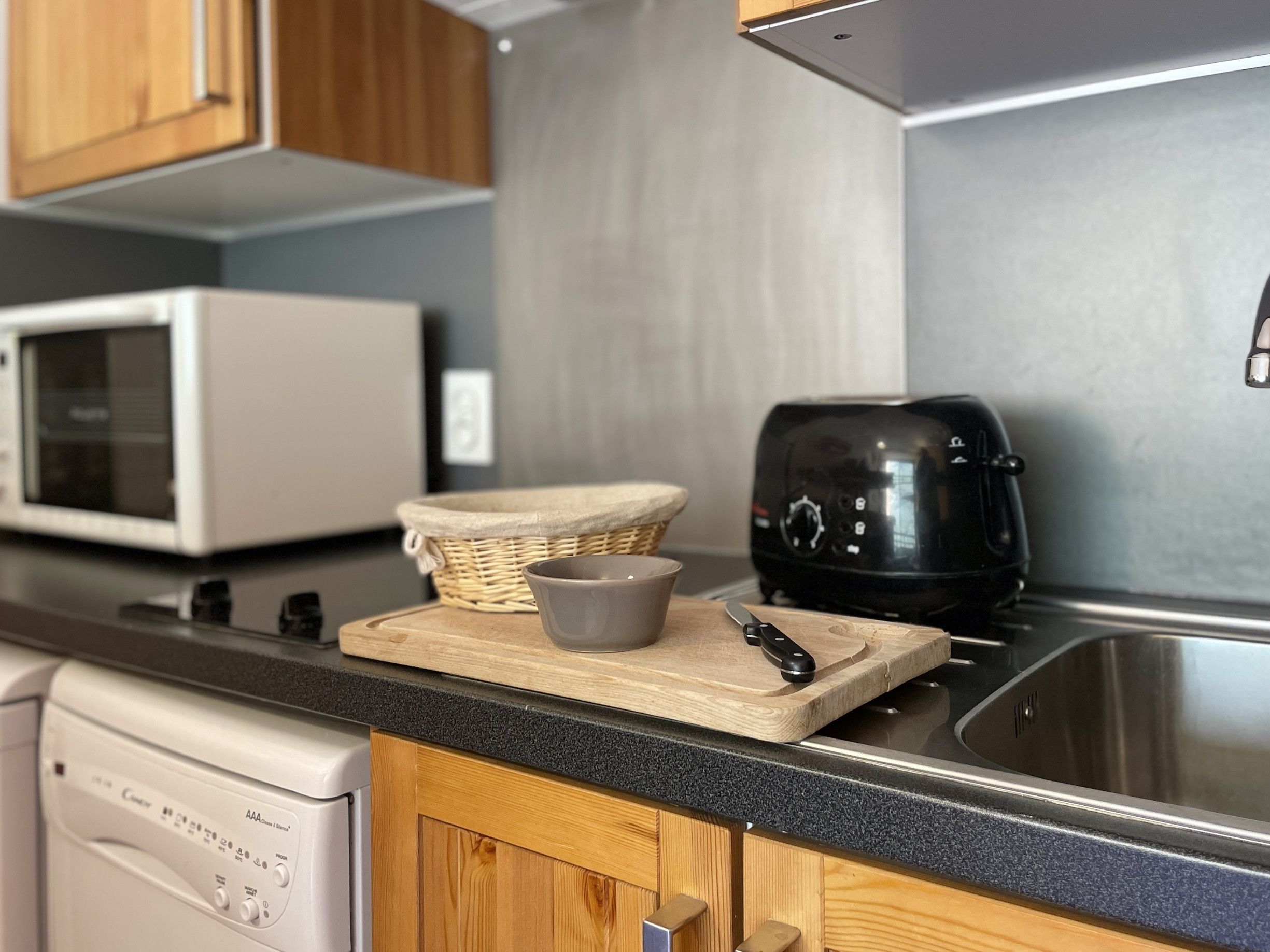 A kitchen with a microwave, toaster, and a wooden cutting board with a bowl and a knife.