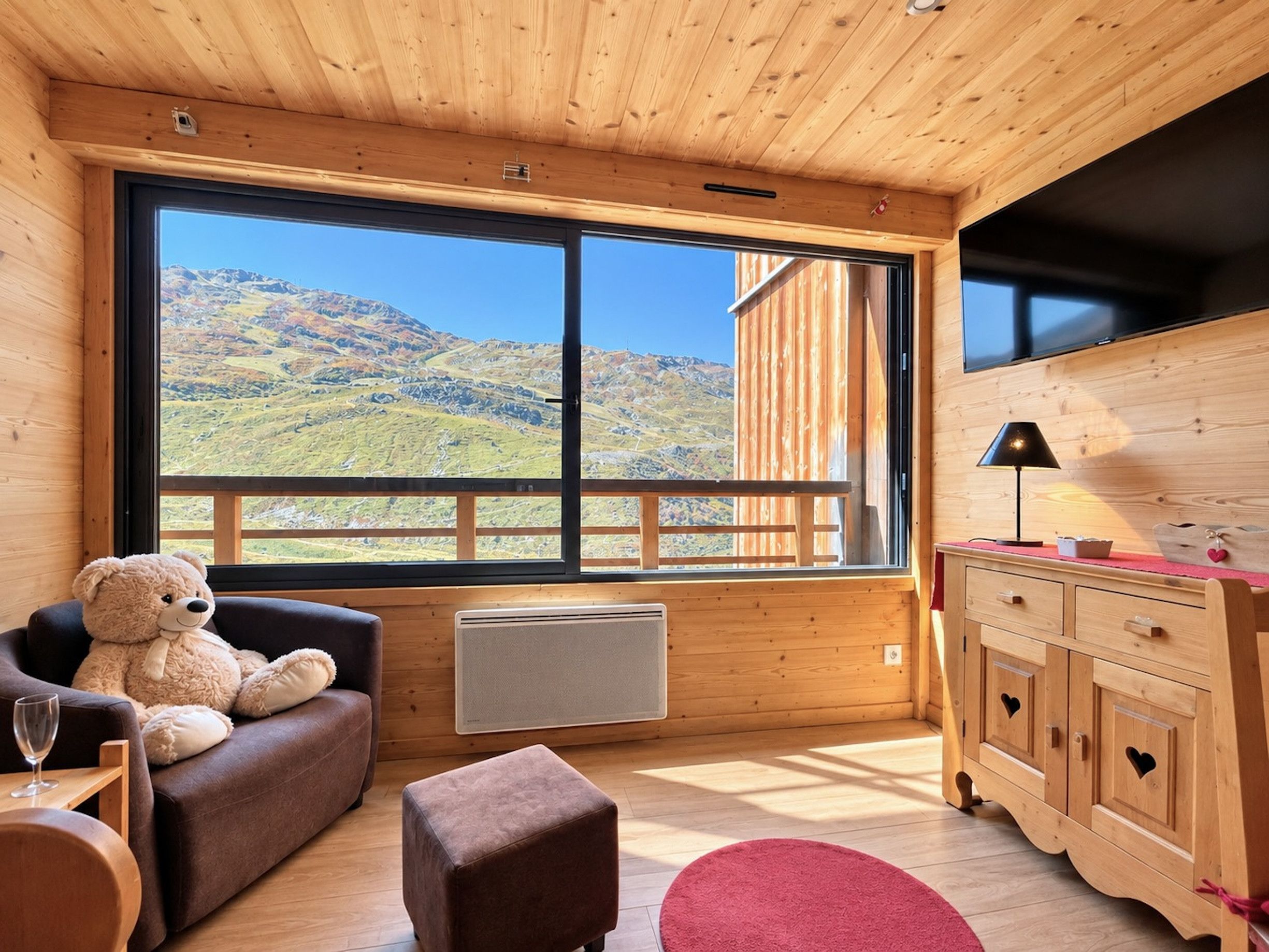 A cozy room with a large window, a sofa, a small table, a lamp, and a cabinet with heart-shaped handles.