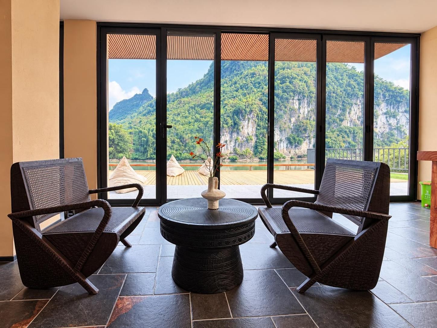 Una habitación con dos sillas de mimbre, una mesa redonda y vistas a un paisaje montañoso a través de amplios ventanales.
