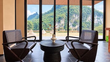 Una habitación con dos sillas de mimbre, una mesa redonda y vistas a un paisaje montañoso a través de amplios ventanales.