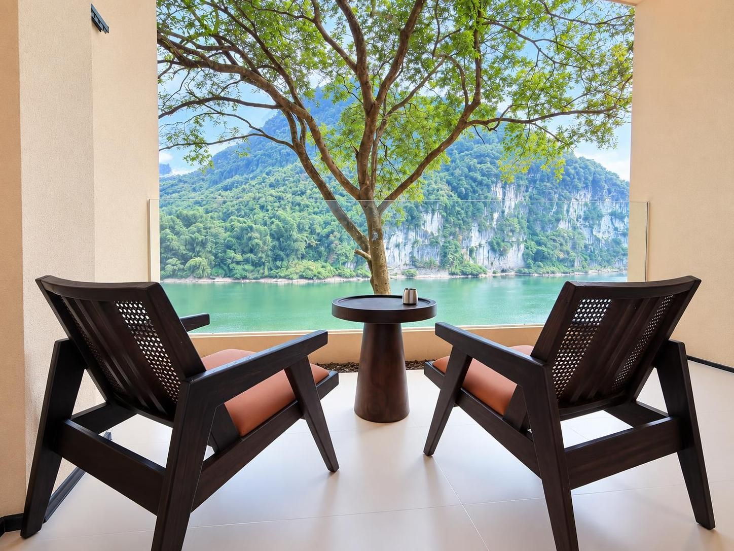 A room with two chairs facing a table, a window with a view of a lake and mountains.