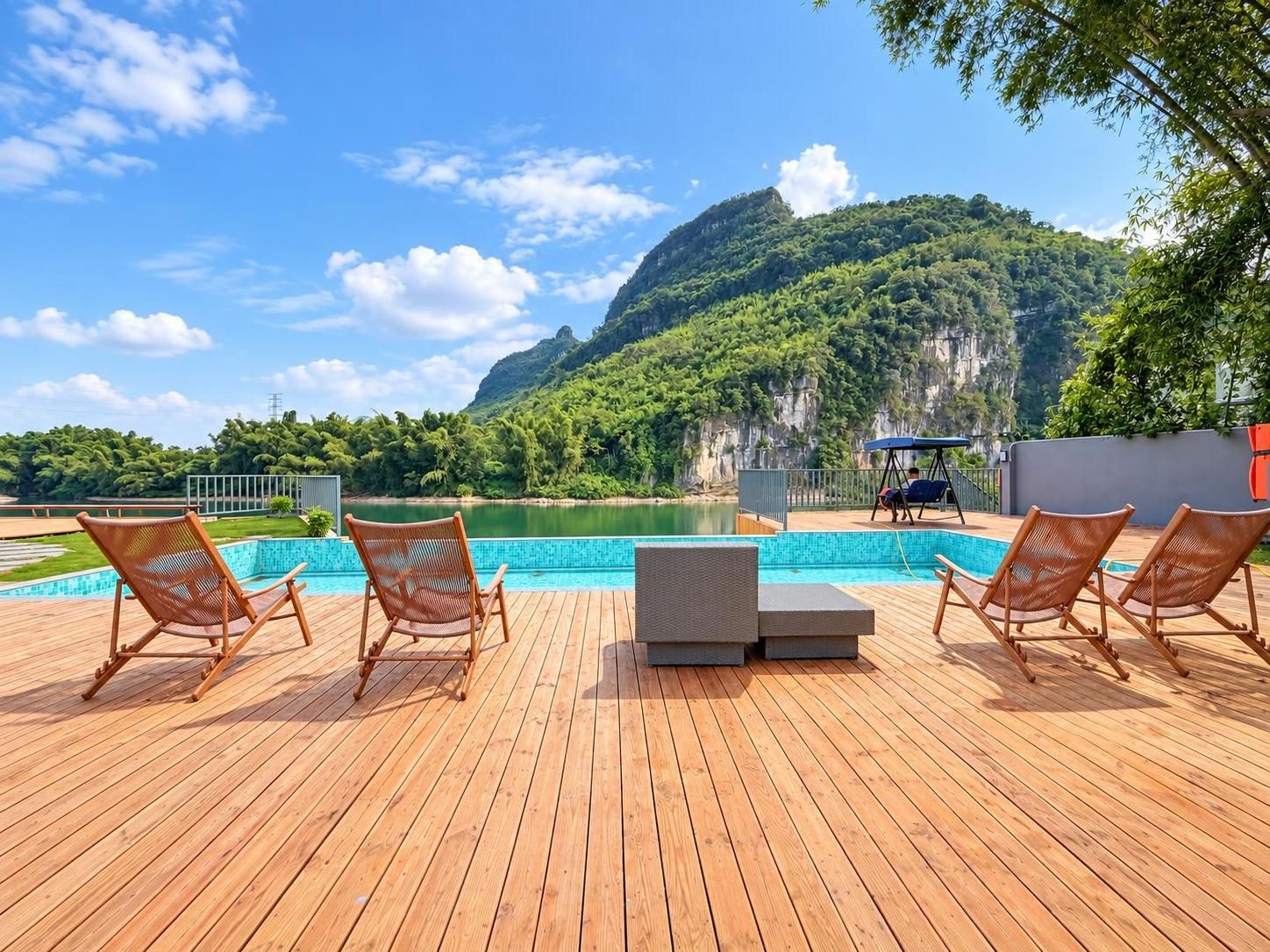 Una terraza de madera con piscina, sillas de descanso y vistas a un lago y montañas.