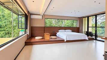 Un dormitorio moderno con una cama grande, un banco de madera y vistas a la vegetación a través de amplios ventanales.