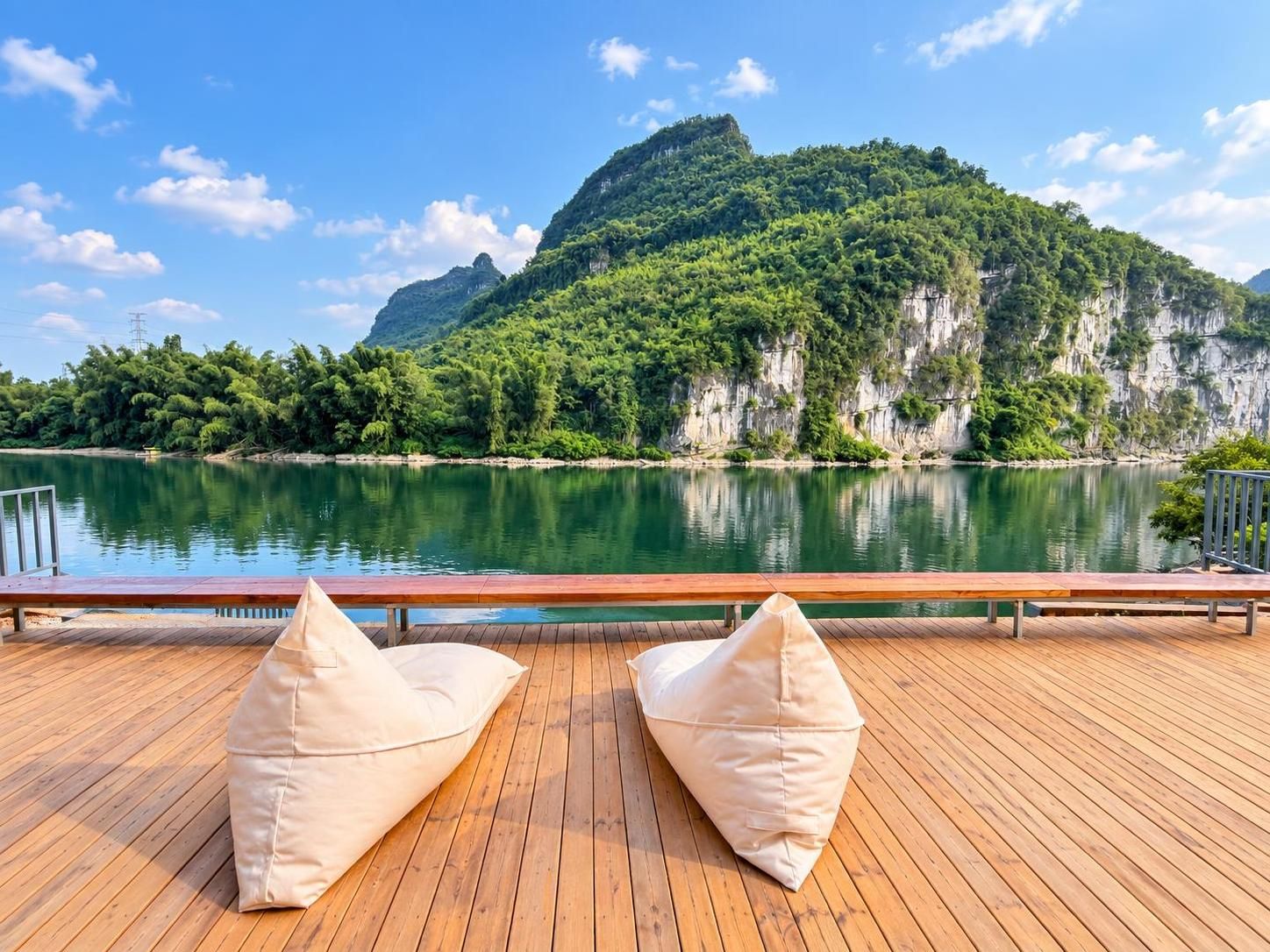 Una terraza de madera con dos bolsas de arena color beige orientadas hacia un lago tranquilo y un paisaje montañoso.