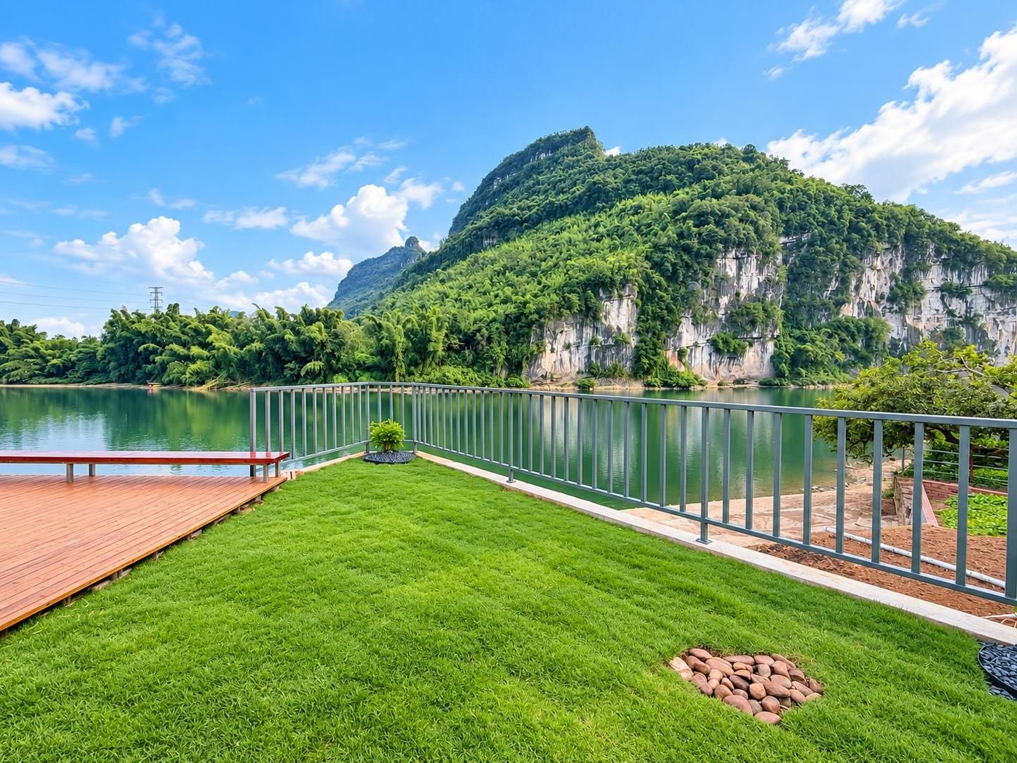 Terraza junto al lago con pasarela de madera, baranda metálica y vista a la montaña.