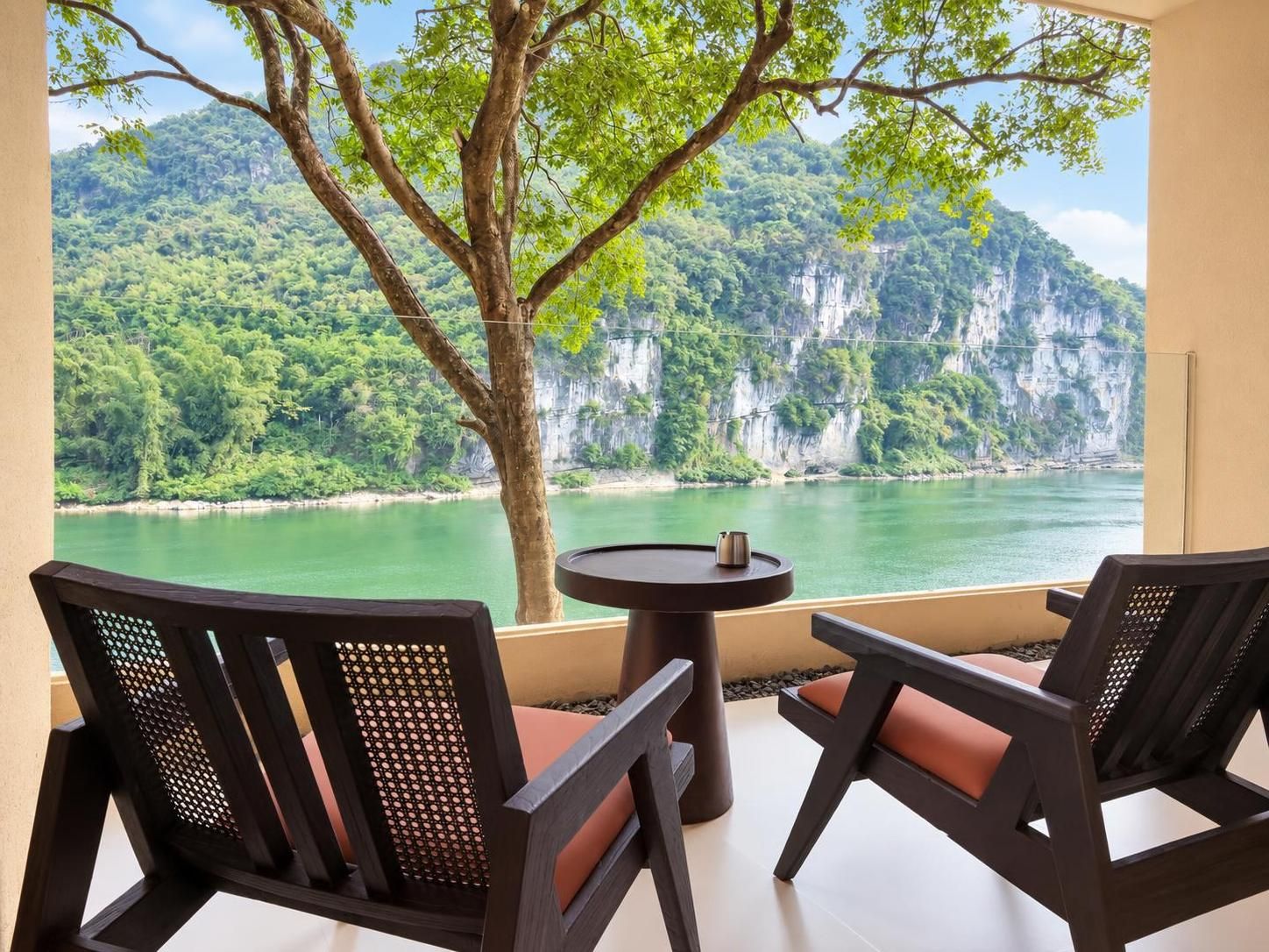 A balcony with two chairs and a table, overlooking a river and cliffs.