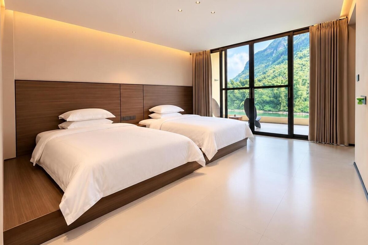 A hotel room with two beds, a large window with a mountain view, and a modern design.