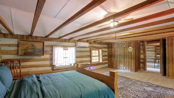 A log cabin room with a bed, two windows, a door, and a mirror.