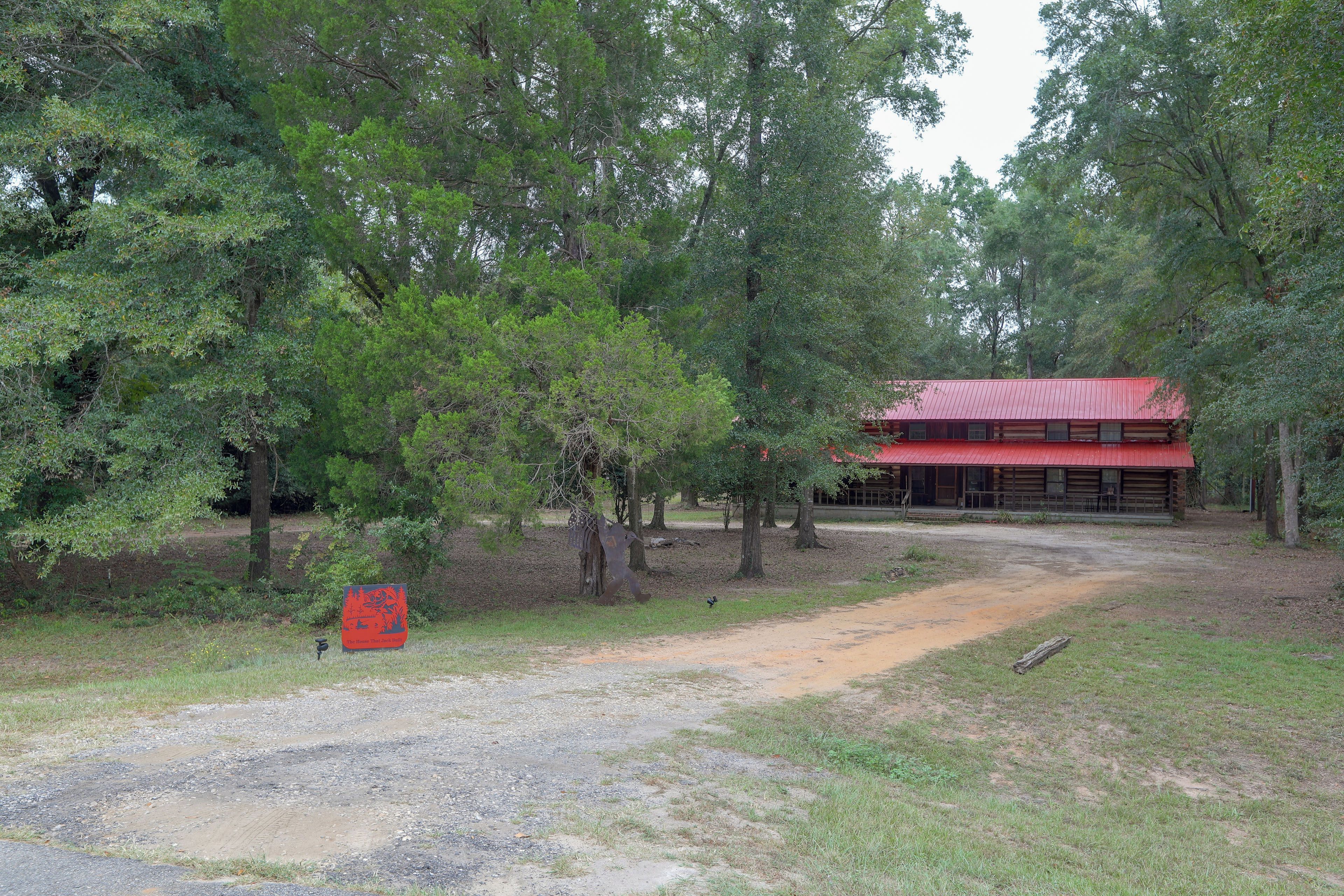 Un bâtiment rustique avec un toit rouge, entouré d’arbres denses et accessible par un chemin de gravier.