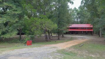 Un bâtiment rustique avec un toit rouge, entouré d’arbres denses et accessible par un chemin de gravier.