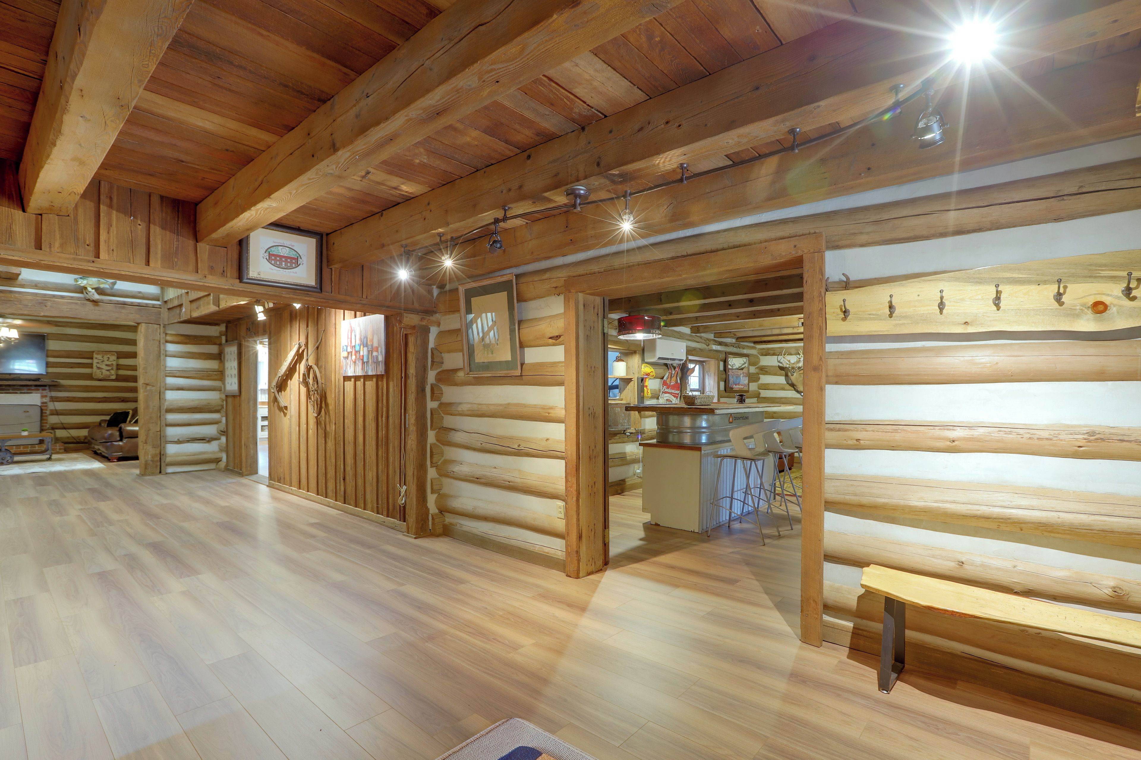 A log cabin interior with wooden walls, a wooden floor, and a bar area with stools.
