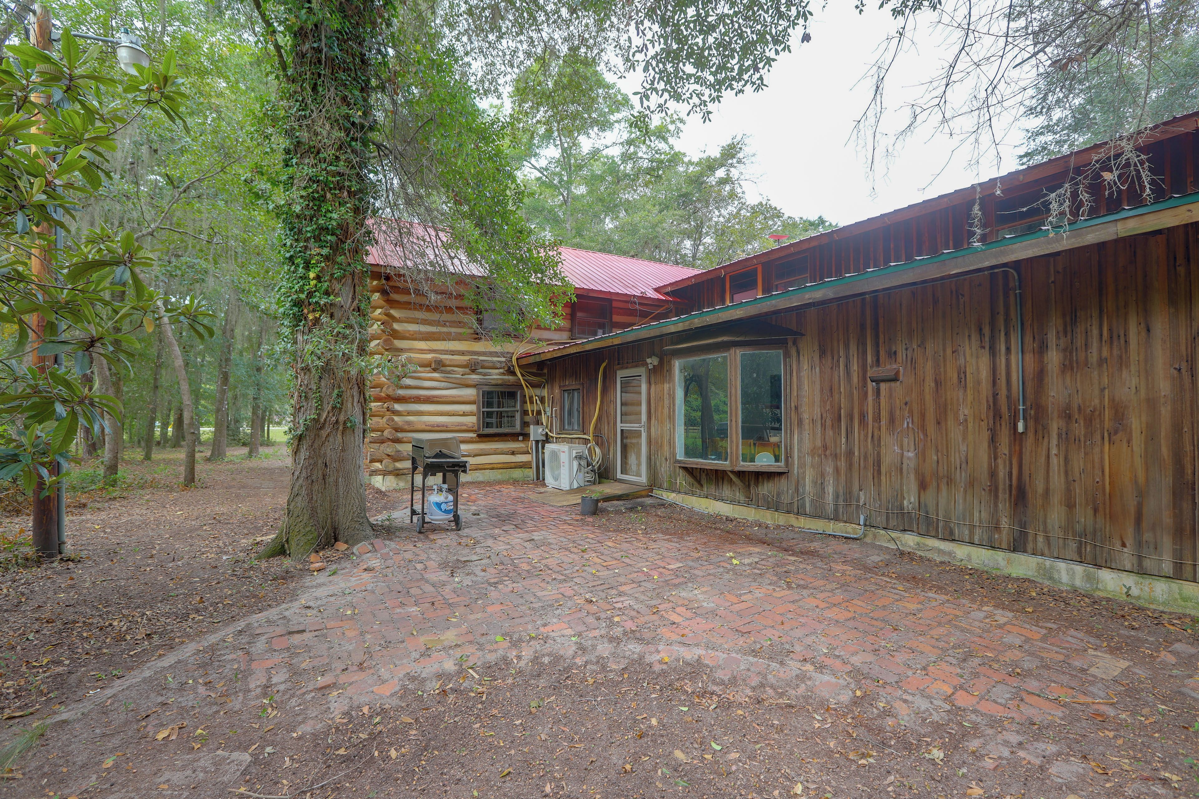 A rustic log cabin with a brick patio, surrounded by trees.