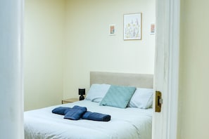 A bedroom with a bed, pillows, a nightstand, and a lamp. - Eurotowers (Gibraltar)