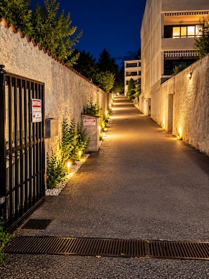 A narrow alleyway with a gated entrance, a metal grate at the bottom, and a building with illuminated windows on the right. - Apartment with a balcony offering mountain views and a pool in a private residence (Introbio)