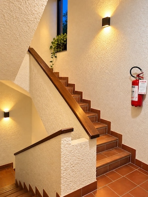A staircase with wooden steps and a handrail, flanked by textured walls and wall-mounted lights. - Apartment with a balcony offering mountain views and a pool in a private residence (Introbio)