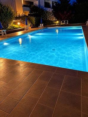 Ein Schwimmbecken mit Fliesen umgeben von Pflanzen und Gartenmöbeln.