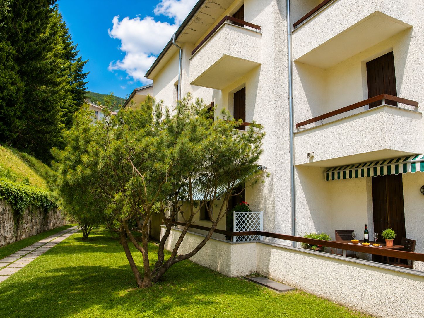 Ein zweigeschossiges Gebäude mit einem Balkon, einer Steinsäule und einem gepflegten Rasen.