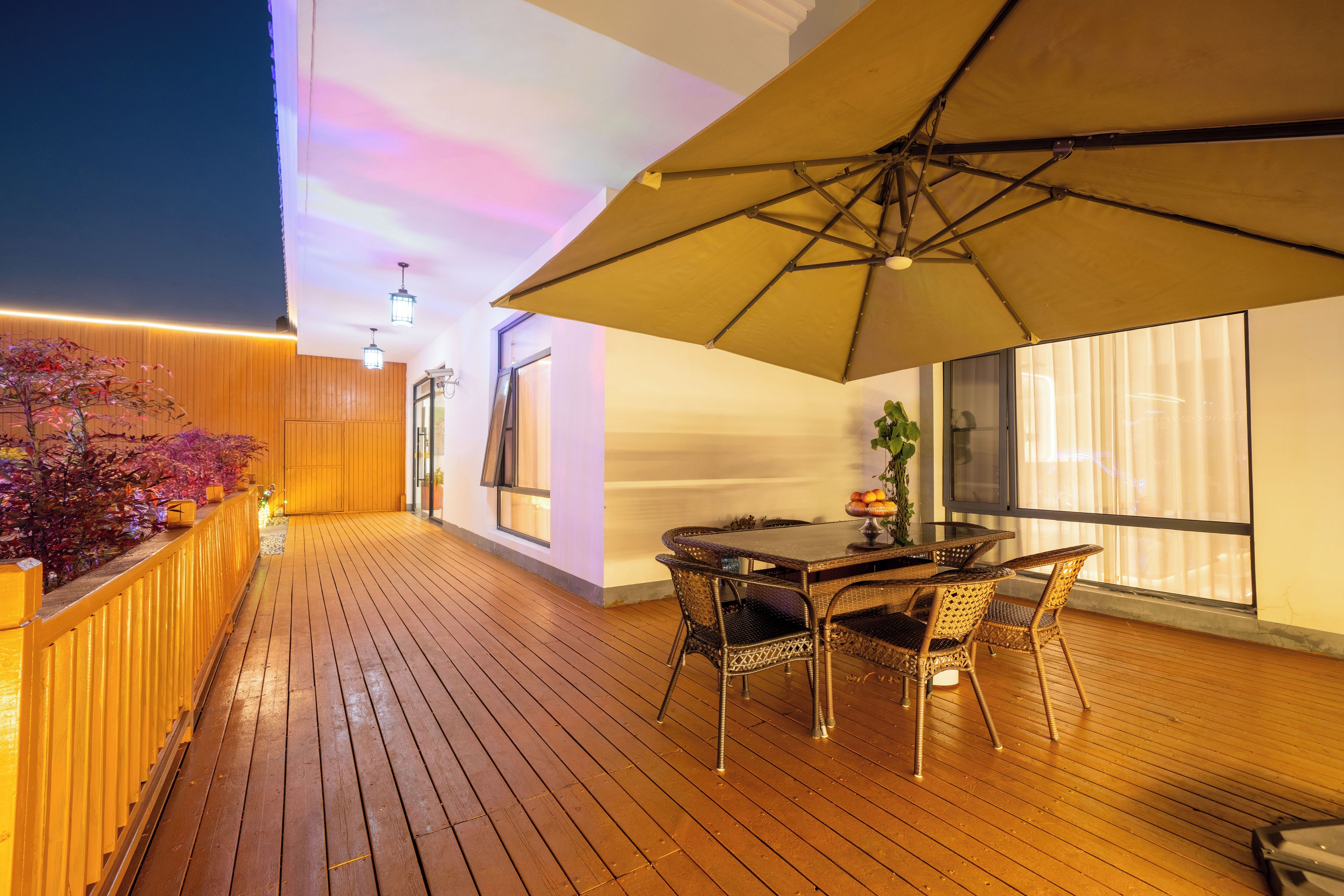 An outdoor wooden deck with a table and chairs, a large umbrella, and a view of the sky.