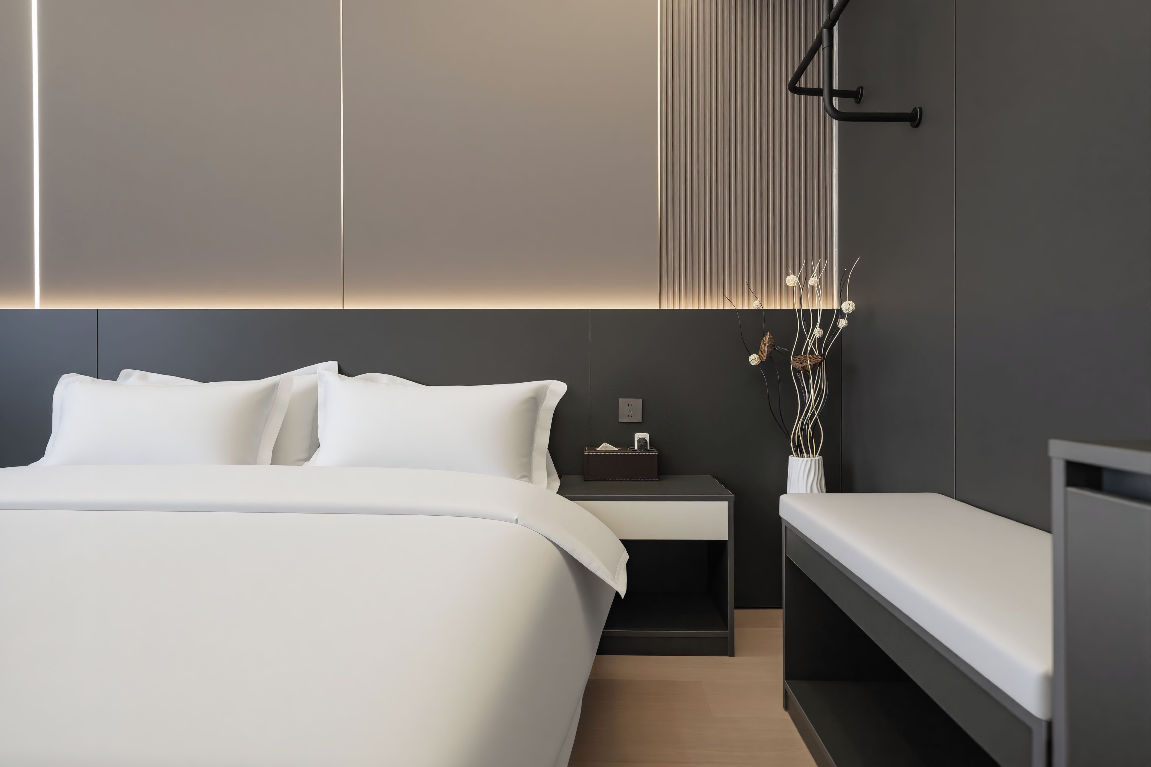 A modern bedroom with a large bed, bedside tables, a nightstand, and a wall-mounted light fixture.