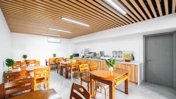 Ein moderner Essbereich mit Holztischen und -stühlen, eine Küche im Hintergrund und eine Decke mit Holzleisten und eingelassener Beleuchtung.