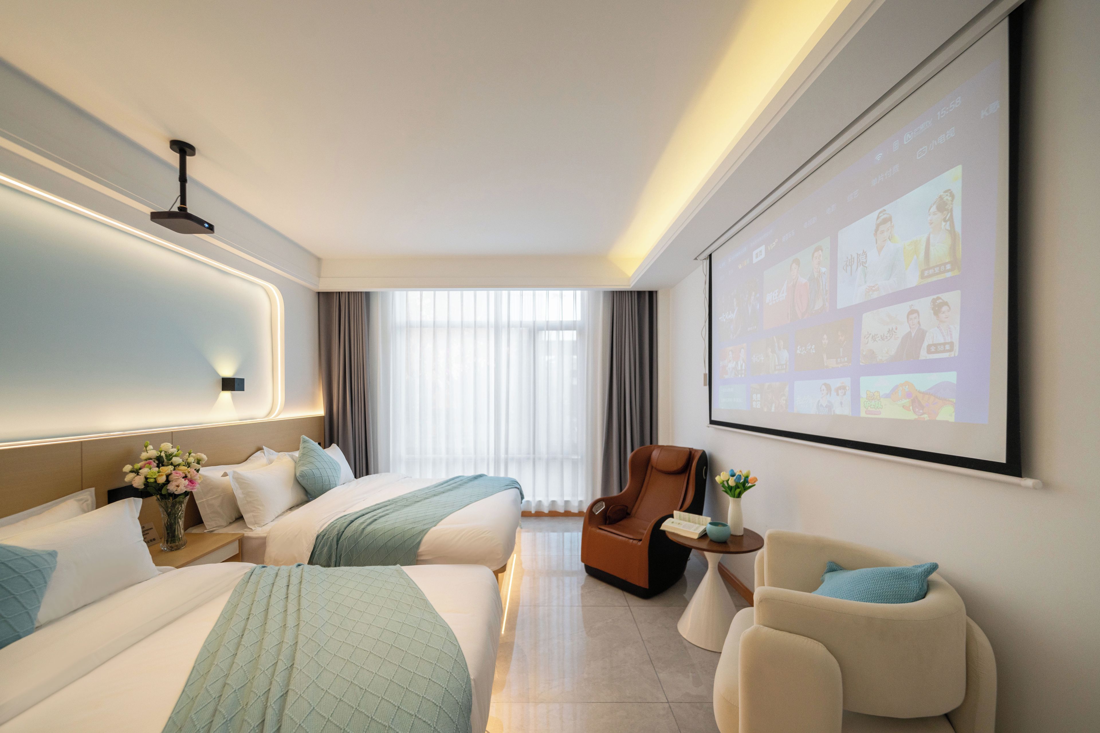 Ein Hotelzimmer mit zwei Betten, einem Massagesessel, einem kleinen Tisch mit einer Vase und einem großen Bildschirm, der Bilder zeigt.