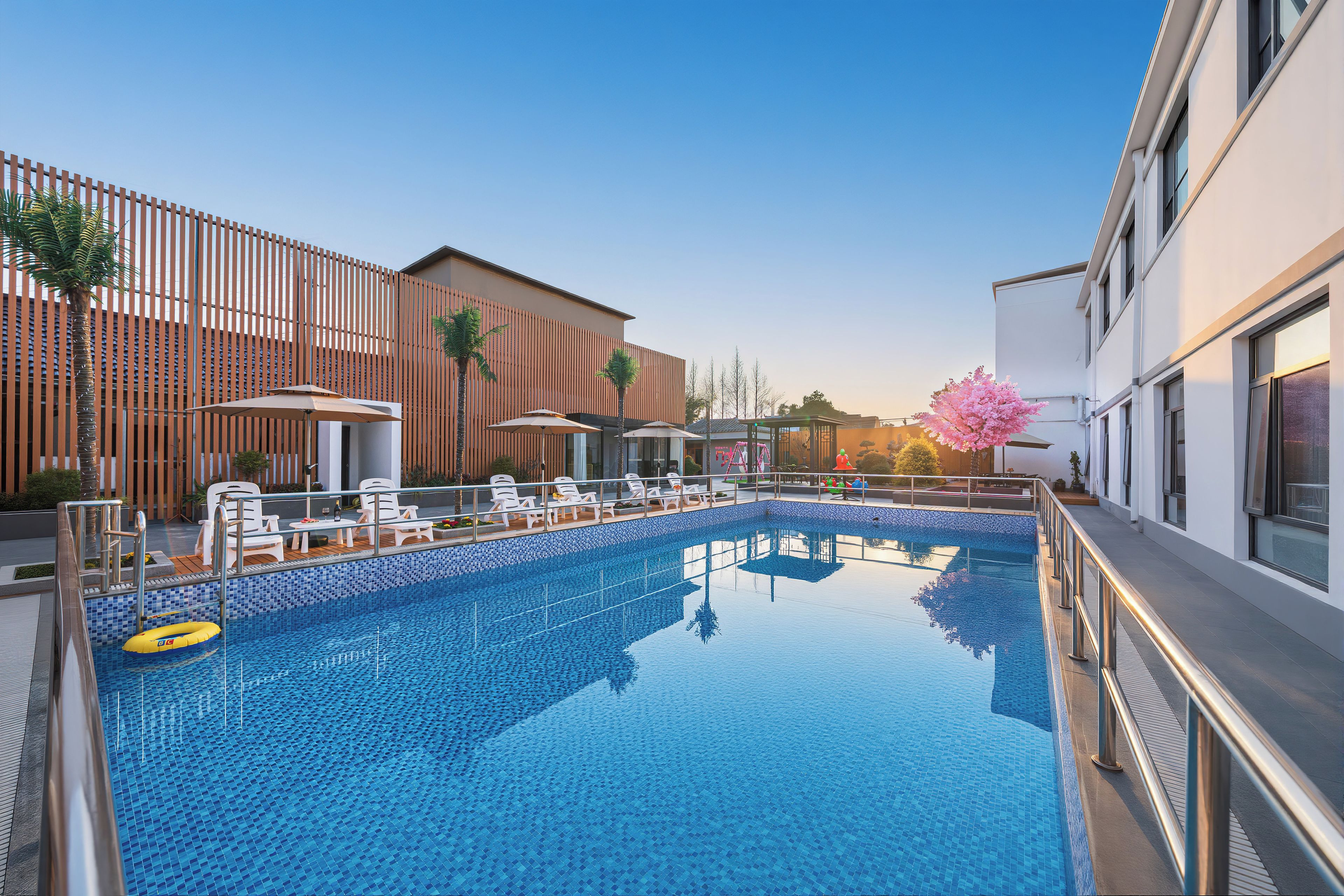 A swimming pool with lounge chairs and umbrellas, surrounded by modern buildings.