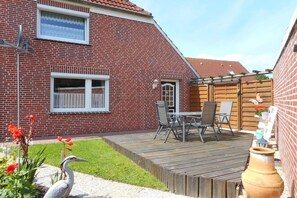 A brick house with a wooden deck, a dining area with chairs, and a bird statue. - Holiday apartment with 2 bedrooms (Krummhörn)