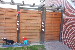 A wooden gate with the word 'MOIN' on it, a small dog, and a person in a red hat pushing a cart. - Holiday apartment with 2 bedrooms (Krummhörn)