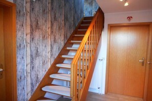 A wooden staircase with white steps and a wooden handrail leading to a door. - Holiday apartment with 2 bedrooms (Krummhörn)