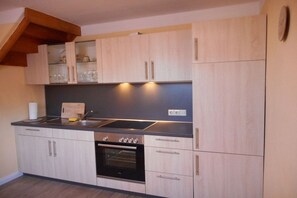 Une cuisine avec des meubles de couleur bois clair, une cuisinière en acier inoxydable et un four encastré.