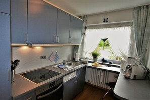 A compact kitchen with a built-in stove, a sink, and a window with curtains. - Alpenflair holiday apartment 202 (Oberstdorf)