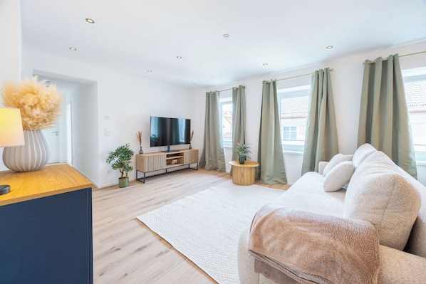 A modern living room with a sofa, TV, and a small wooden table. - Simply Stay Homes Bergliebe & Seeglück (Traunstein)