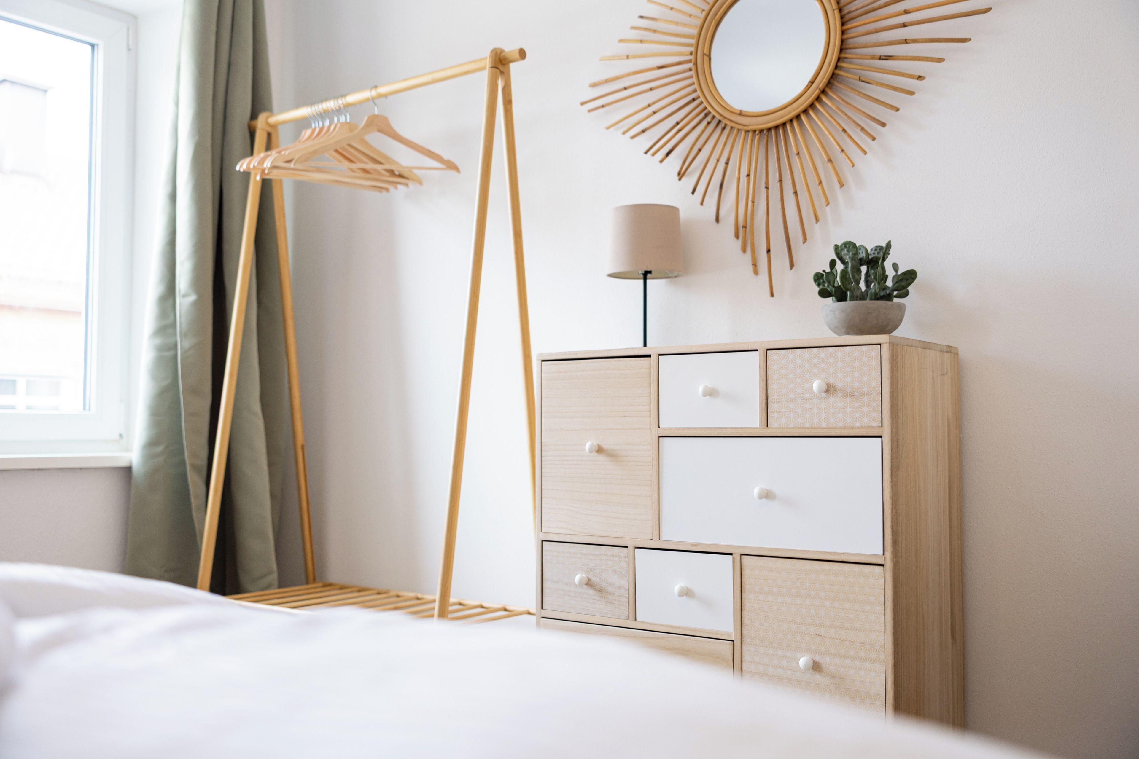 Ein ordentlich eingerichtetes Schlafzimmer mit einem Holzschrank, einer Kleiderstange, einem Wandspiegel und einer Nachttischlampe.