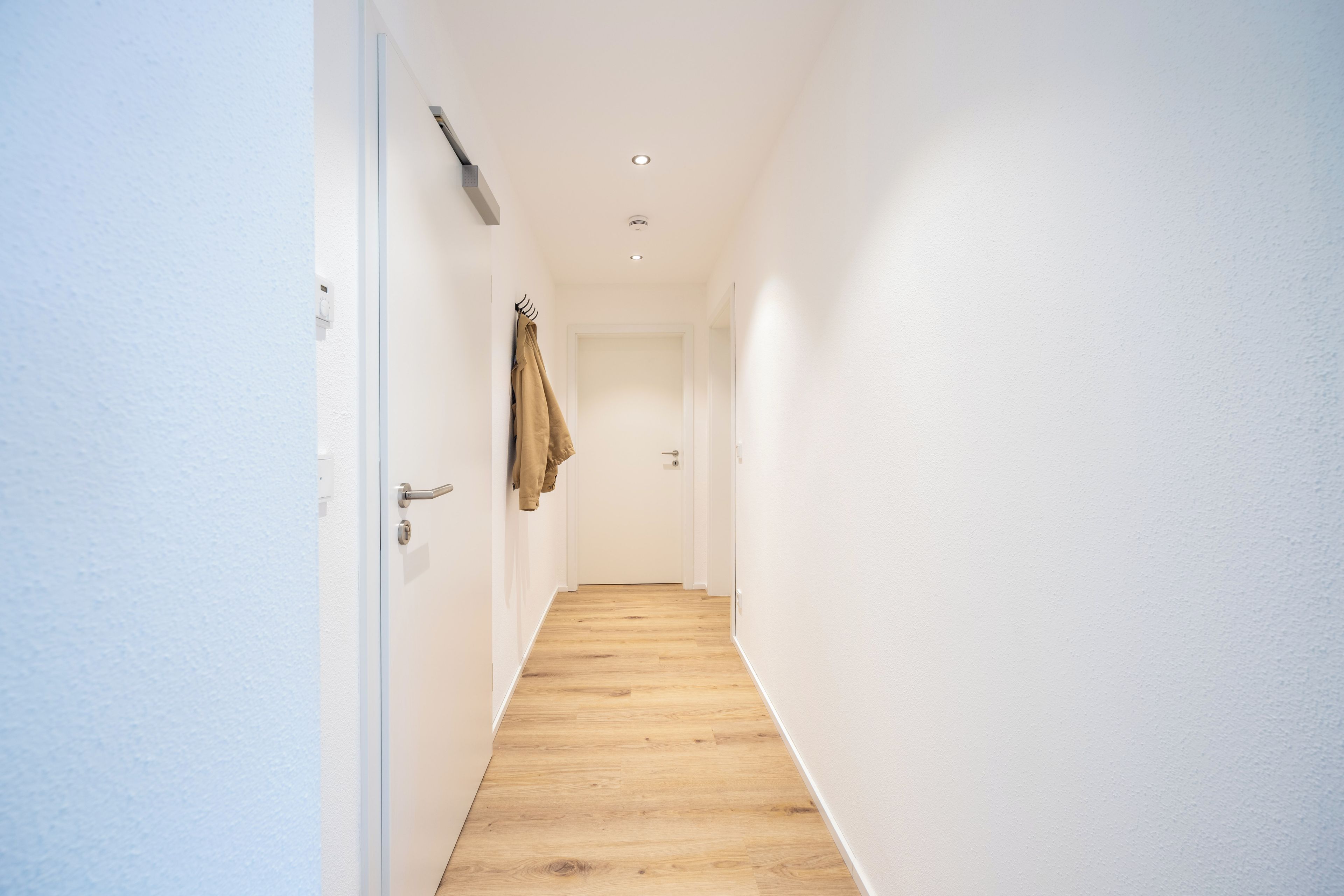 A narrow hallway with wooden flooring and white walls.