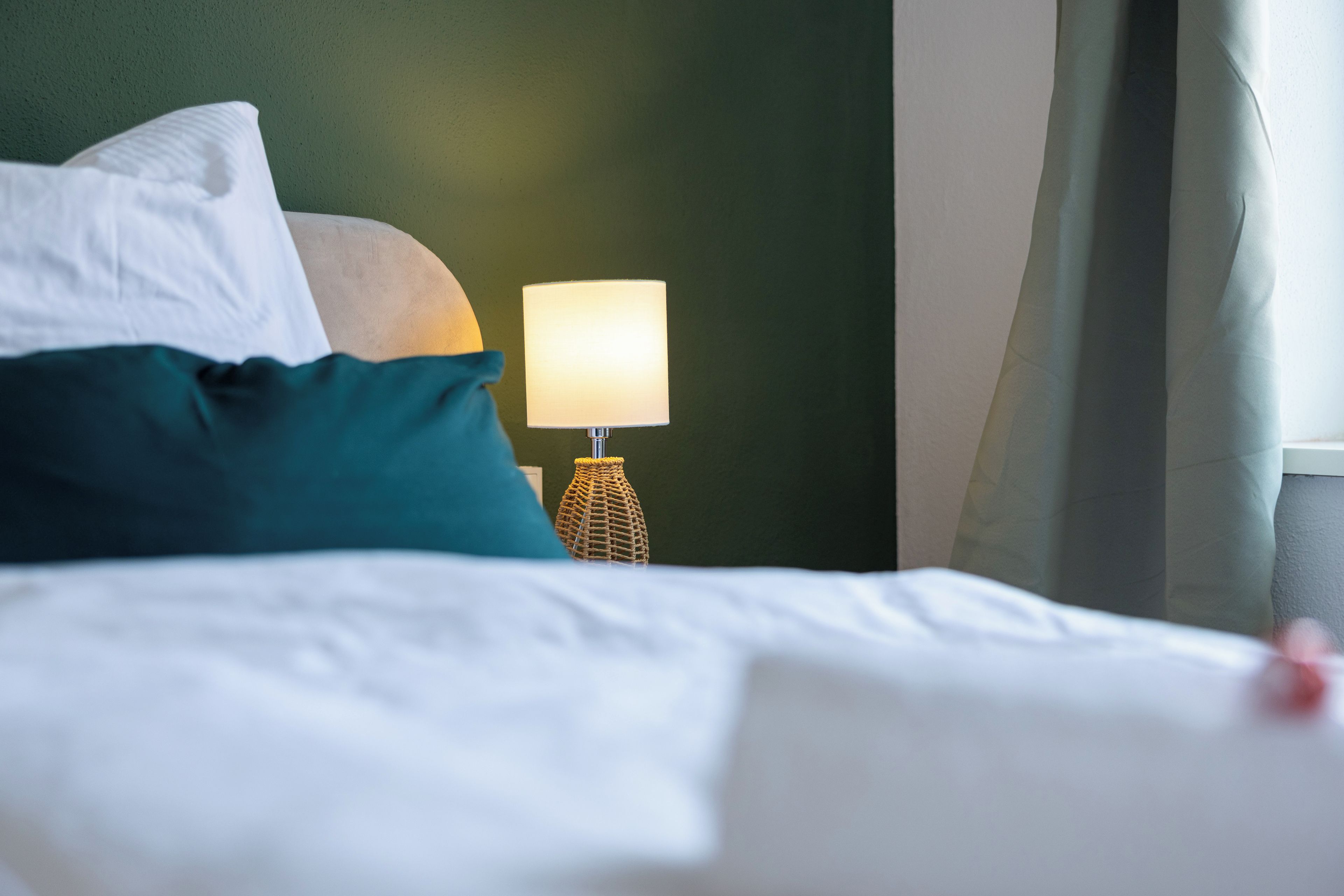 A neatly made bed with white linens and a teal pillow.