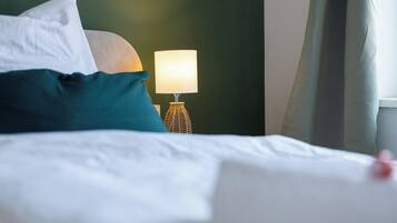 A neatly made bed with white linens and a teal pillow.